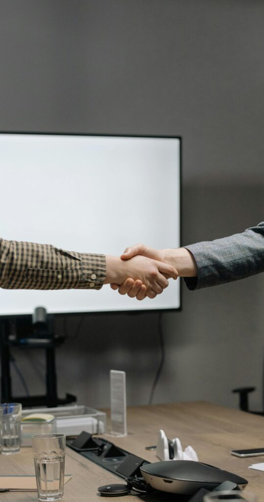 Two business professionals shaking hands in a modern meeting room, symbolizing successful collaboration.